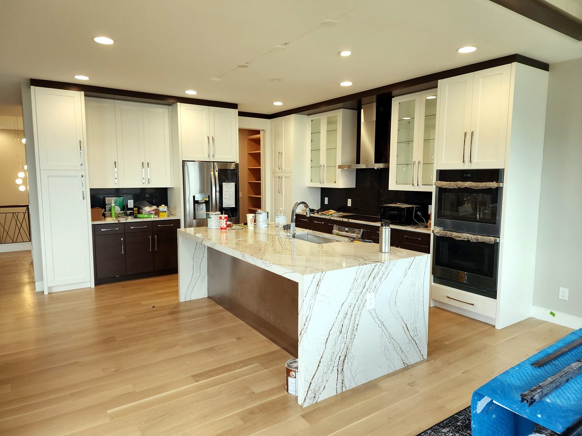 Open kitchen with white shaker cabinets, dark espresso base cabinets, and a dramatic marble waterfall island