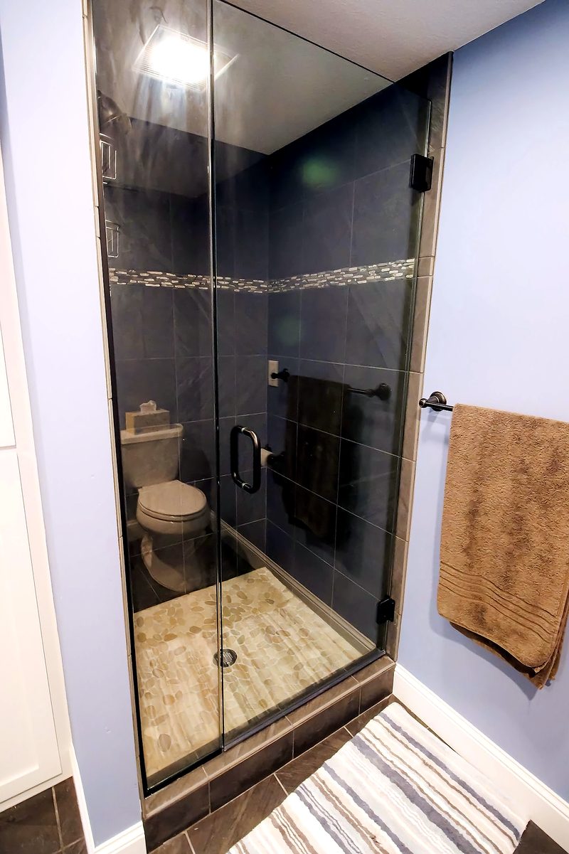 Basement full bath with dark porcelain tile, glass shower, and pebble floor