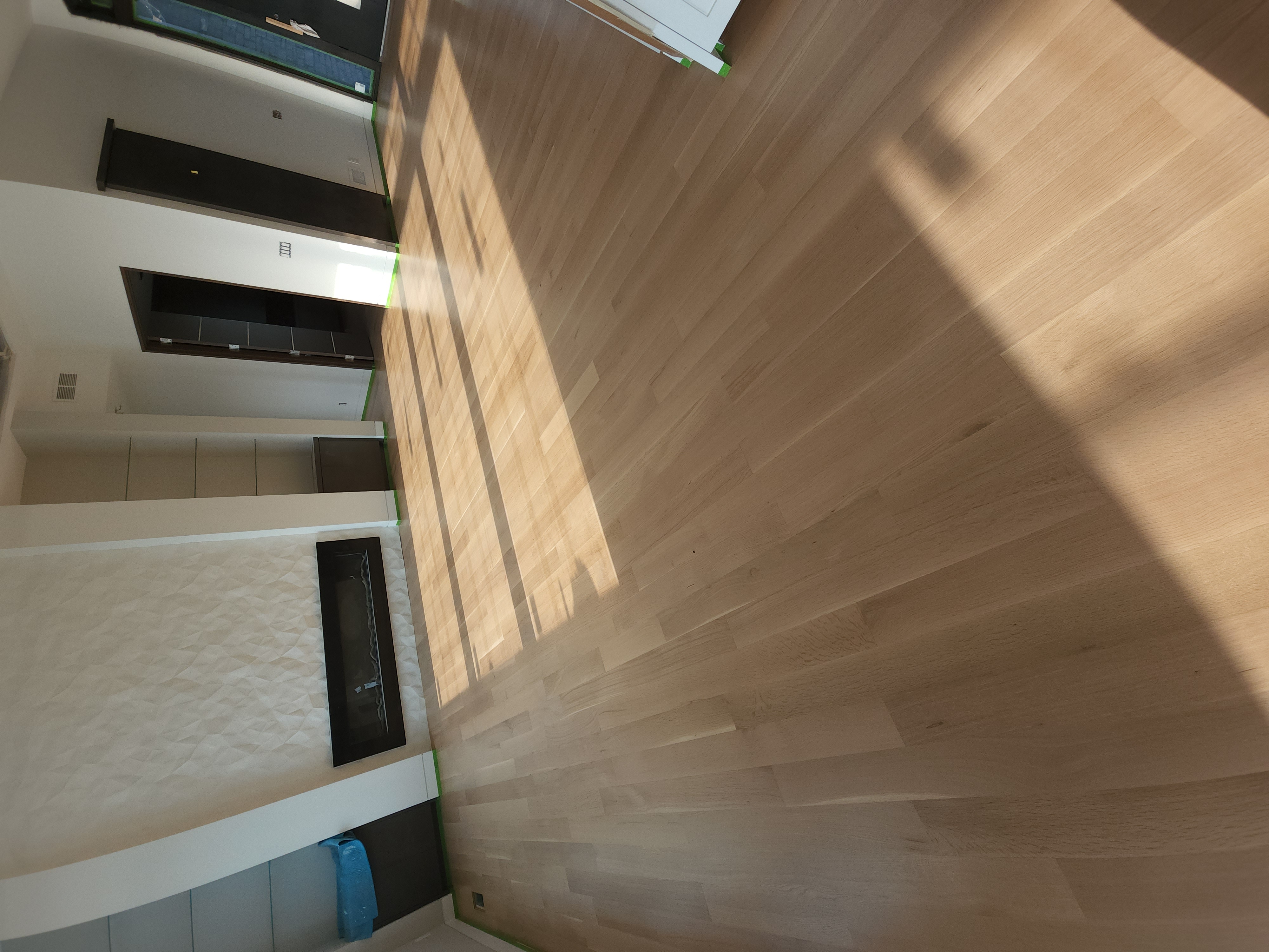 Great room with wide-plank light wood floors, linear fireplace, and textured feature wall with strong natural light.