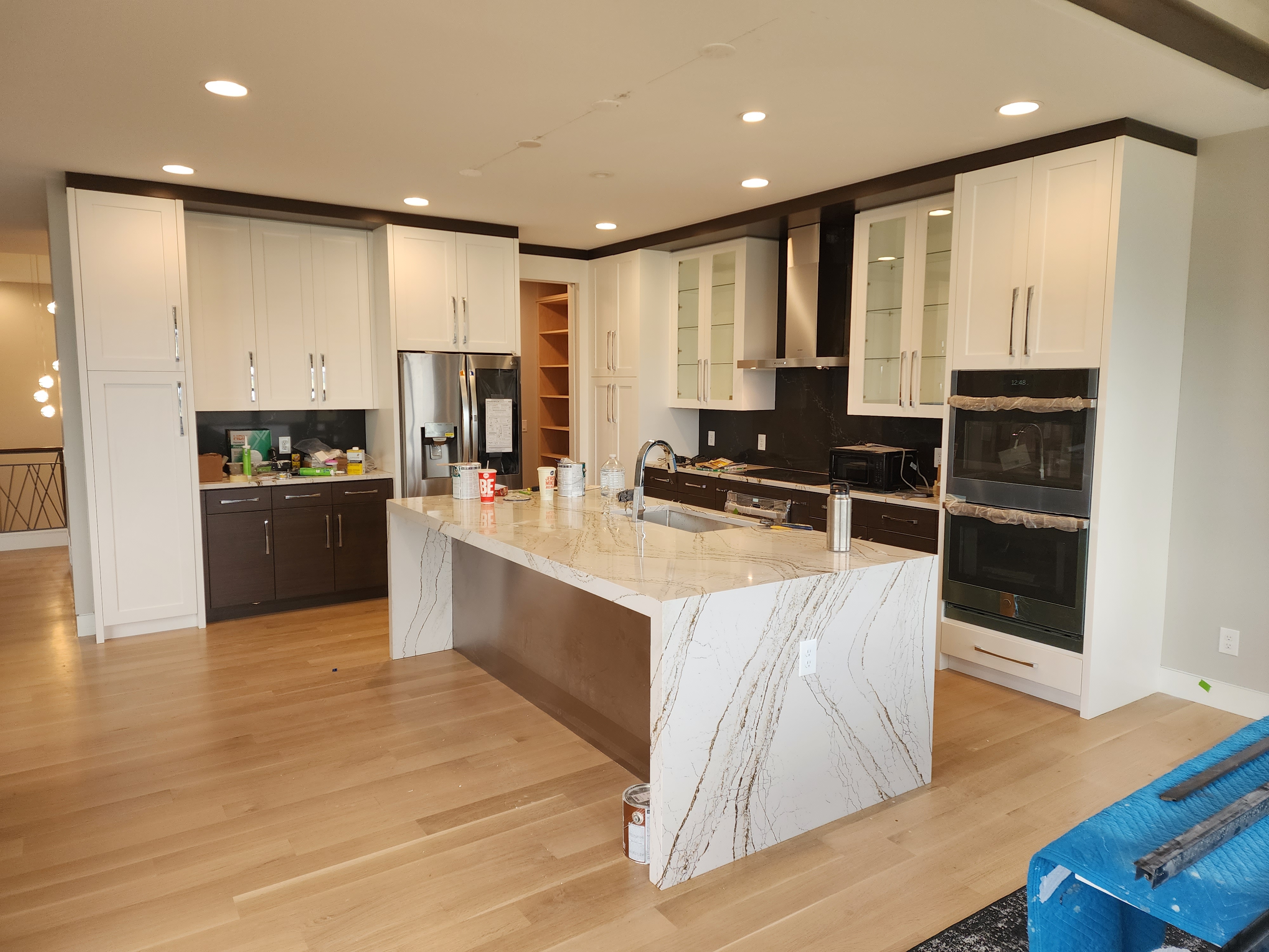 Open-concept kitchen with waterfall quartz island, two-tone cabinetry, built-in appliances, and recessed lighting.