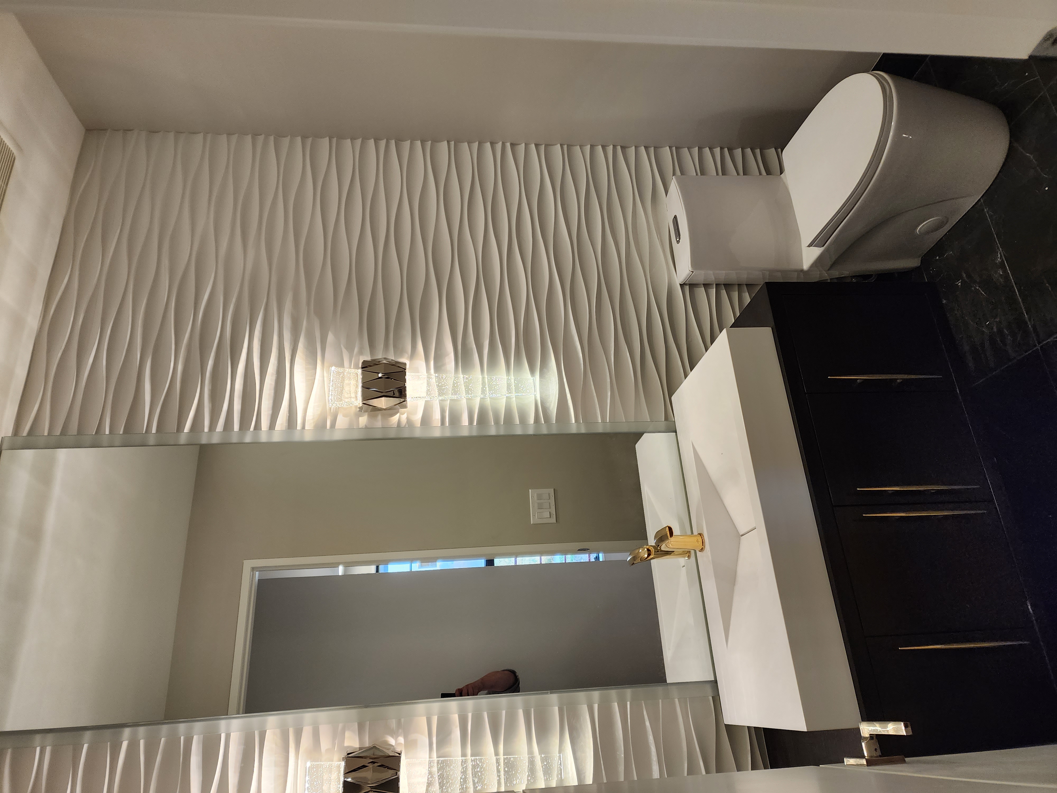 Powder bath with dark vanity, sculpted sink, brass faucet, tall mirror, and textured wall panels.
