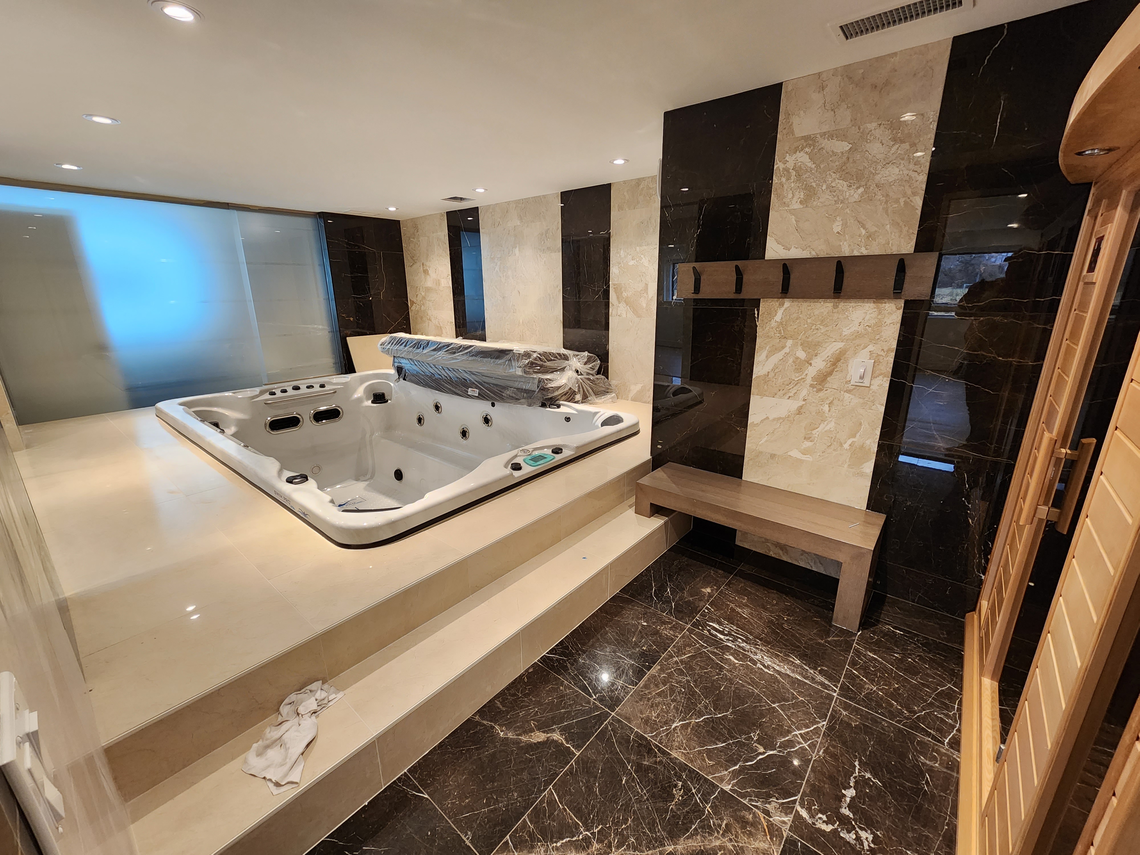 Spa room with raised hot tub, sauna entry, large-format tile walls, and built-in bench seating.