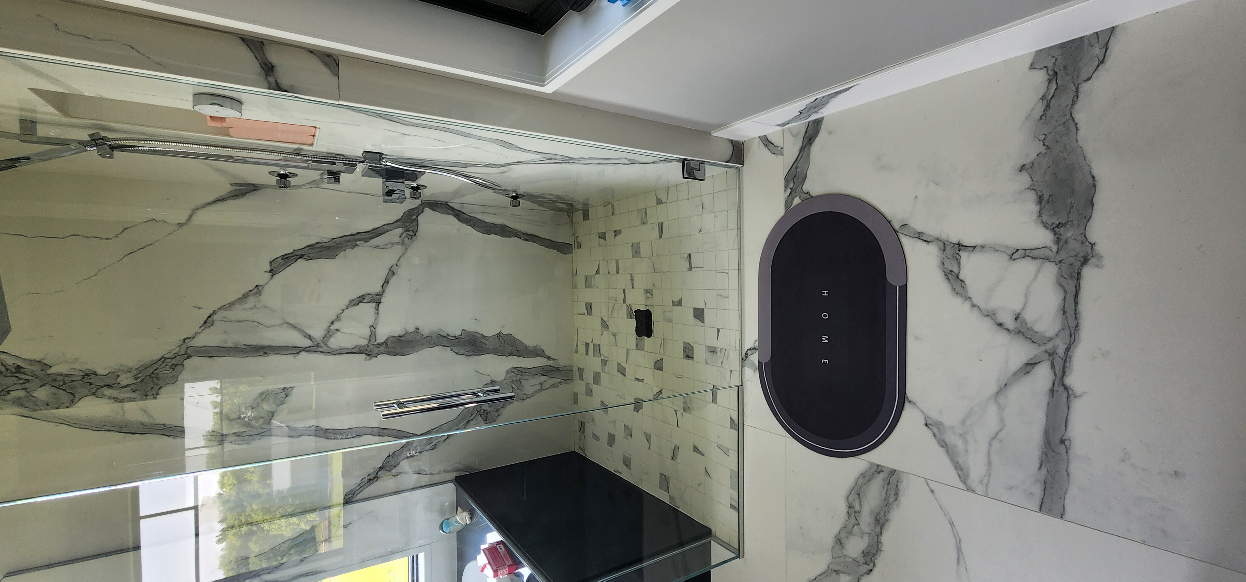 Walk-in shower with full-height marble-look slab walls, frameless glass enclosure, and multi-spray shower fixtures.