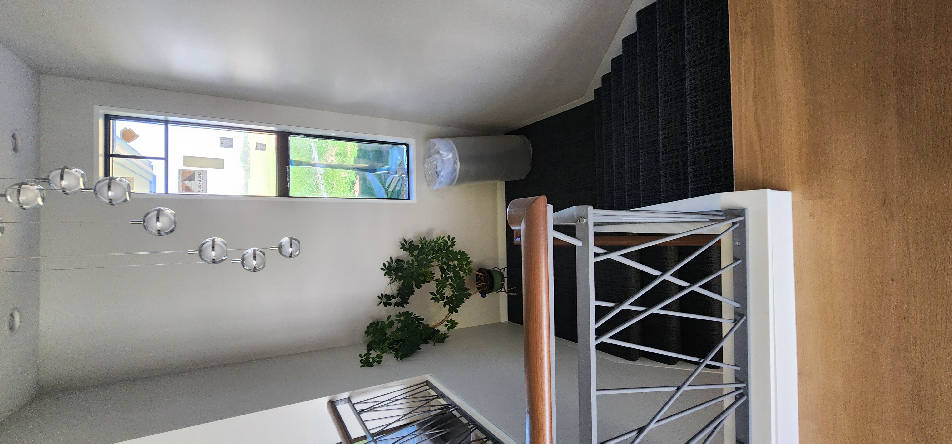 Stairwell view with modern iron railing, carpeted stairs, tall window, and pendant lighting overhead.