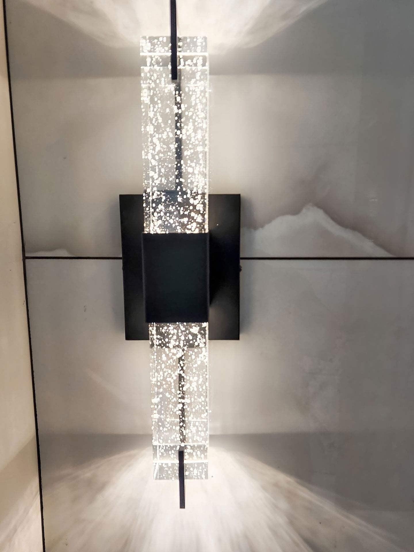 Modern wall sconce detail with clear textured glass and black mounting plate.