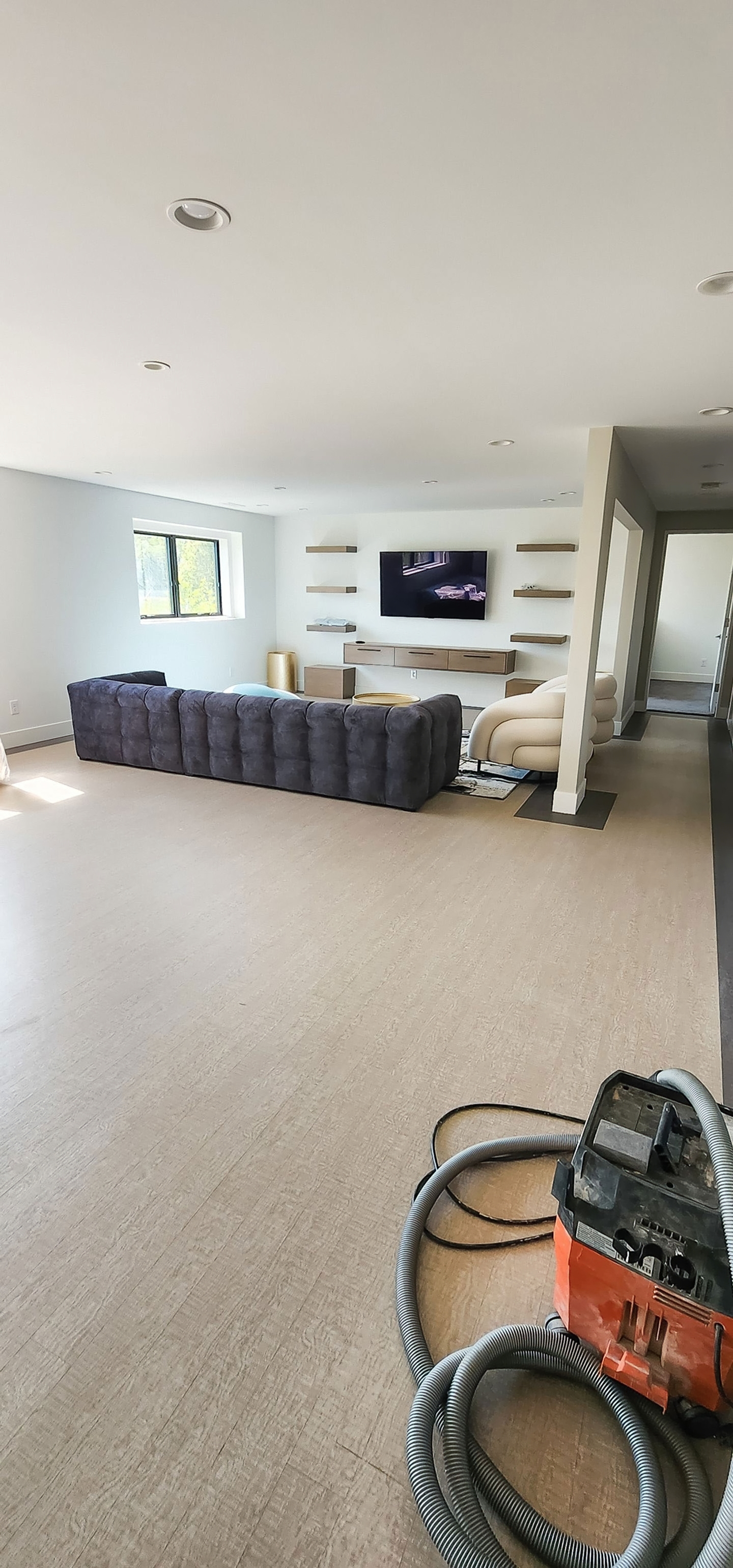 Lower-level living area with wall-mounted TV, floating shelves, and lounge seating in a bright, open space.