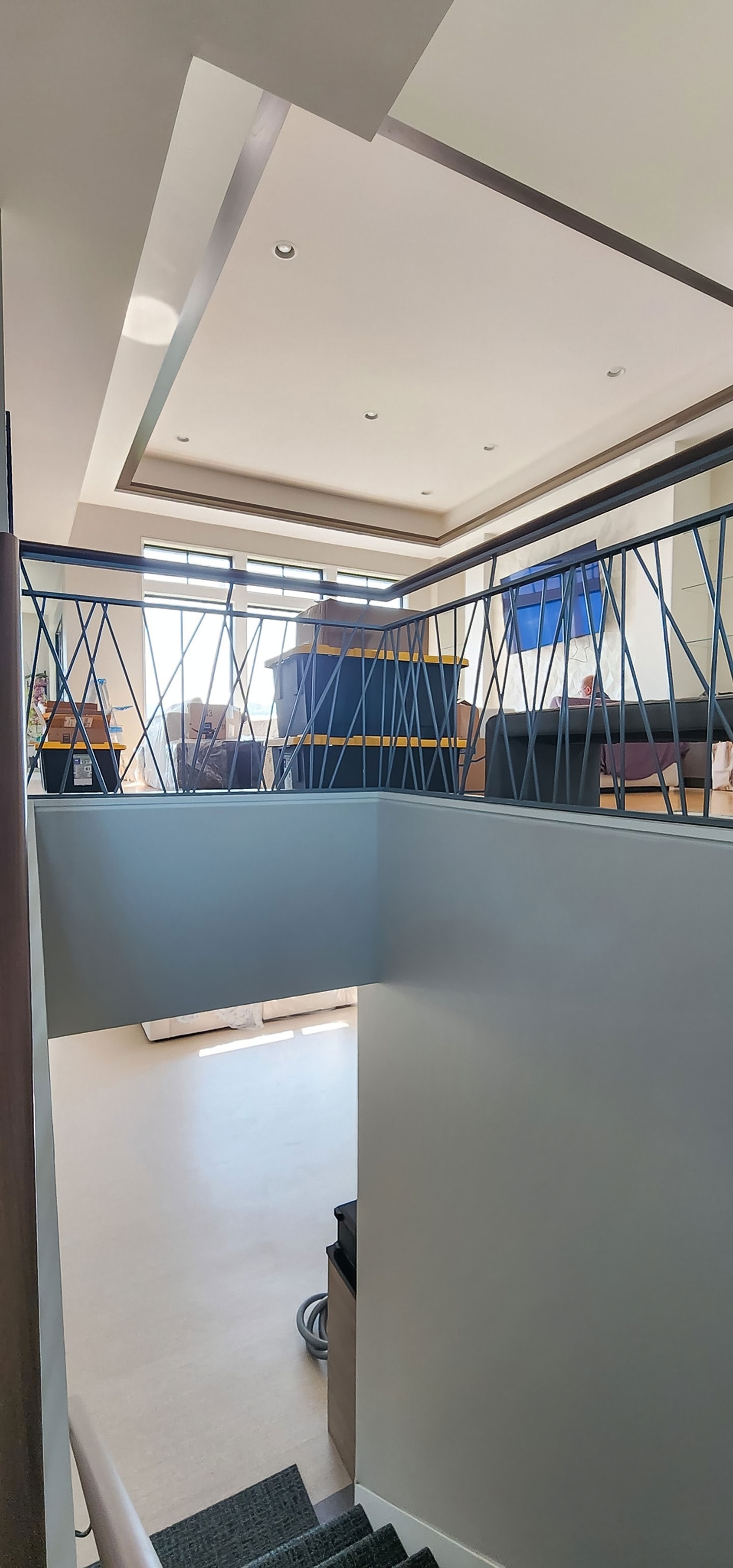 Upper-level overlook with modern iron railing and tray ceiling, opening to the main living area below.