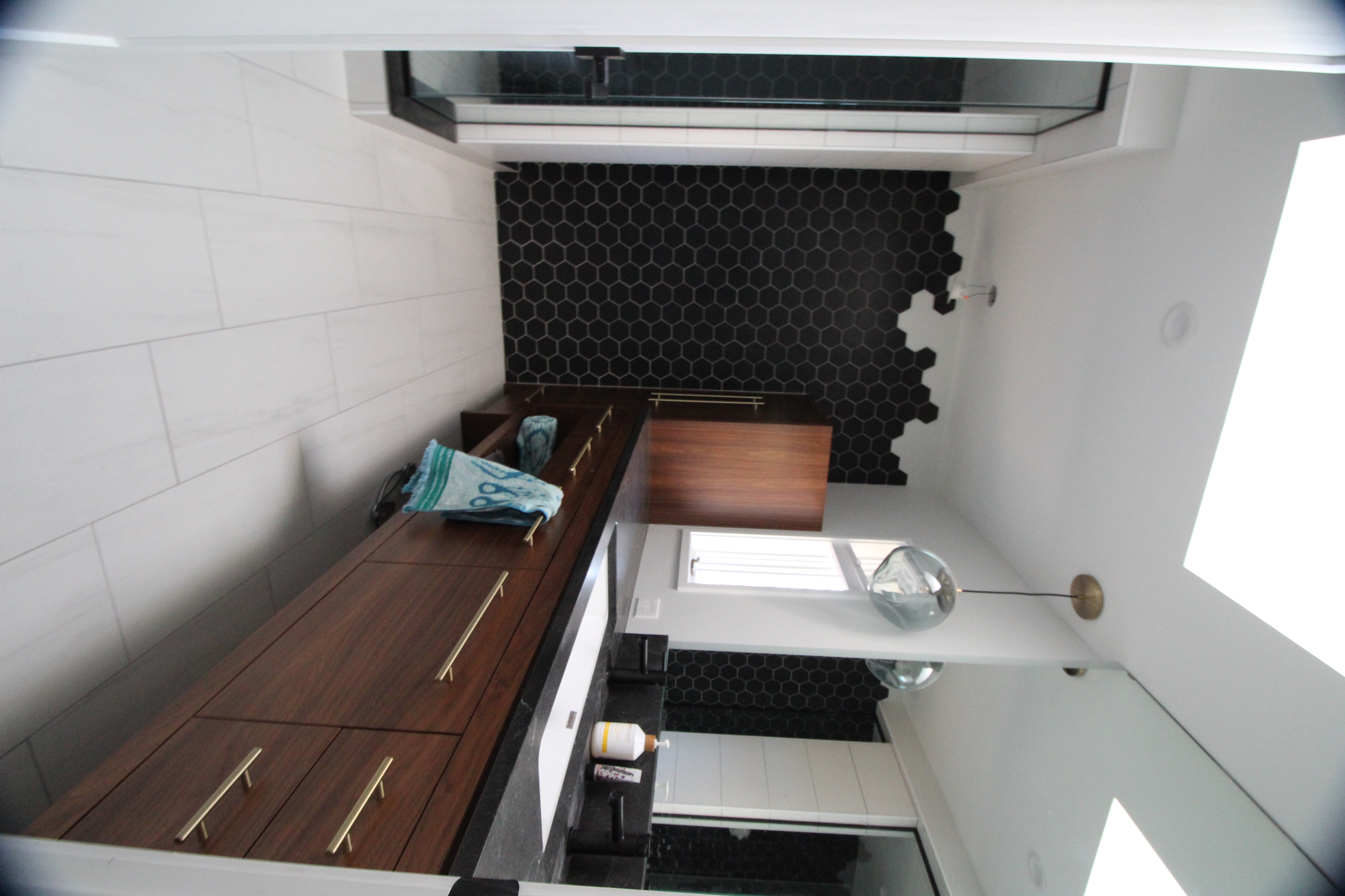 Contemporary bathroom with long walnut vanity, brass hardware, and black hex tile accent wall.