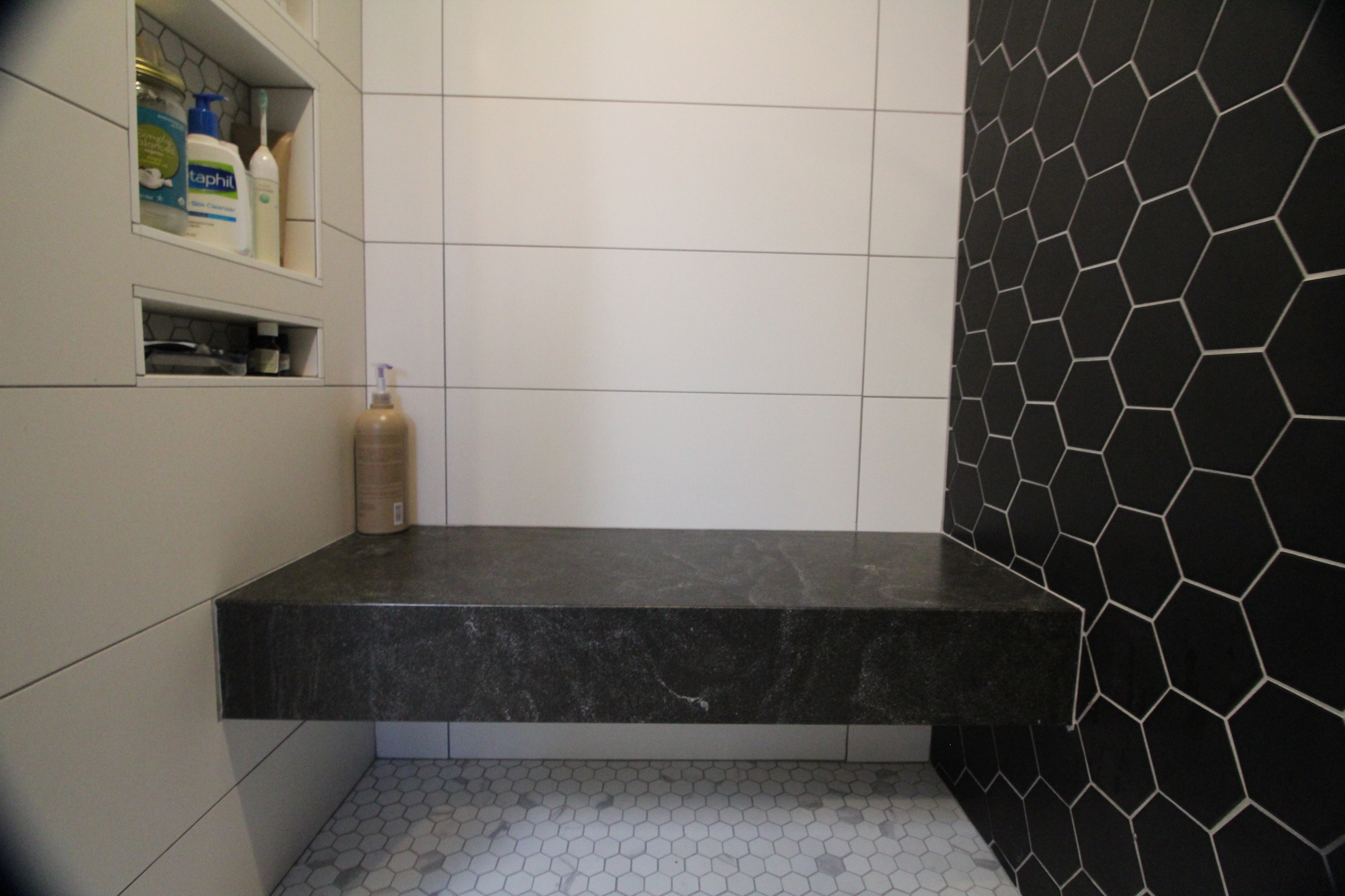 Shower niche and floating stone bench with white wall tile and black hex tile feature.