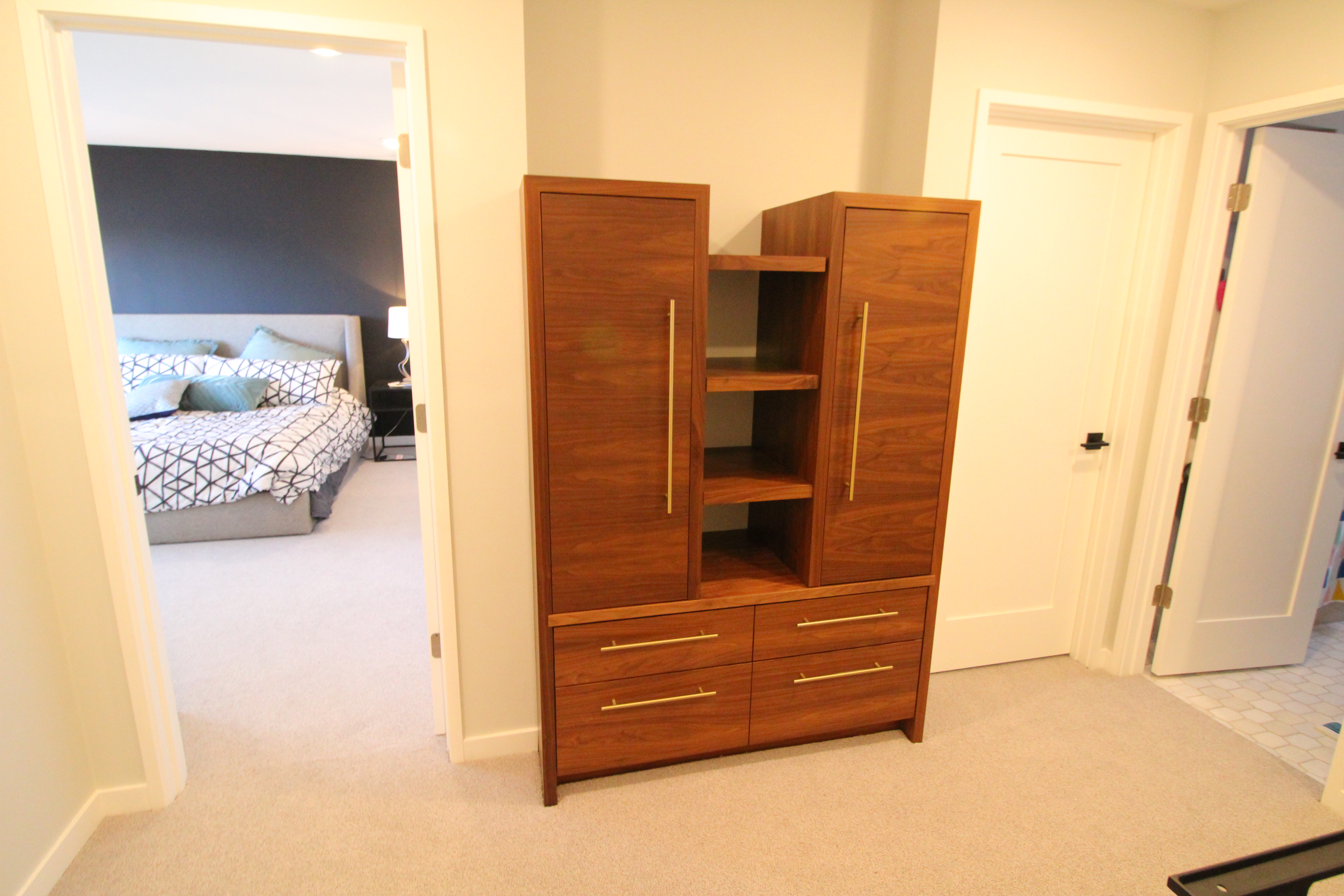 Custom walnut built-in wardrobe cabinet with long brass pulls and open shelving.