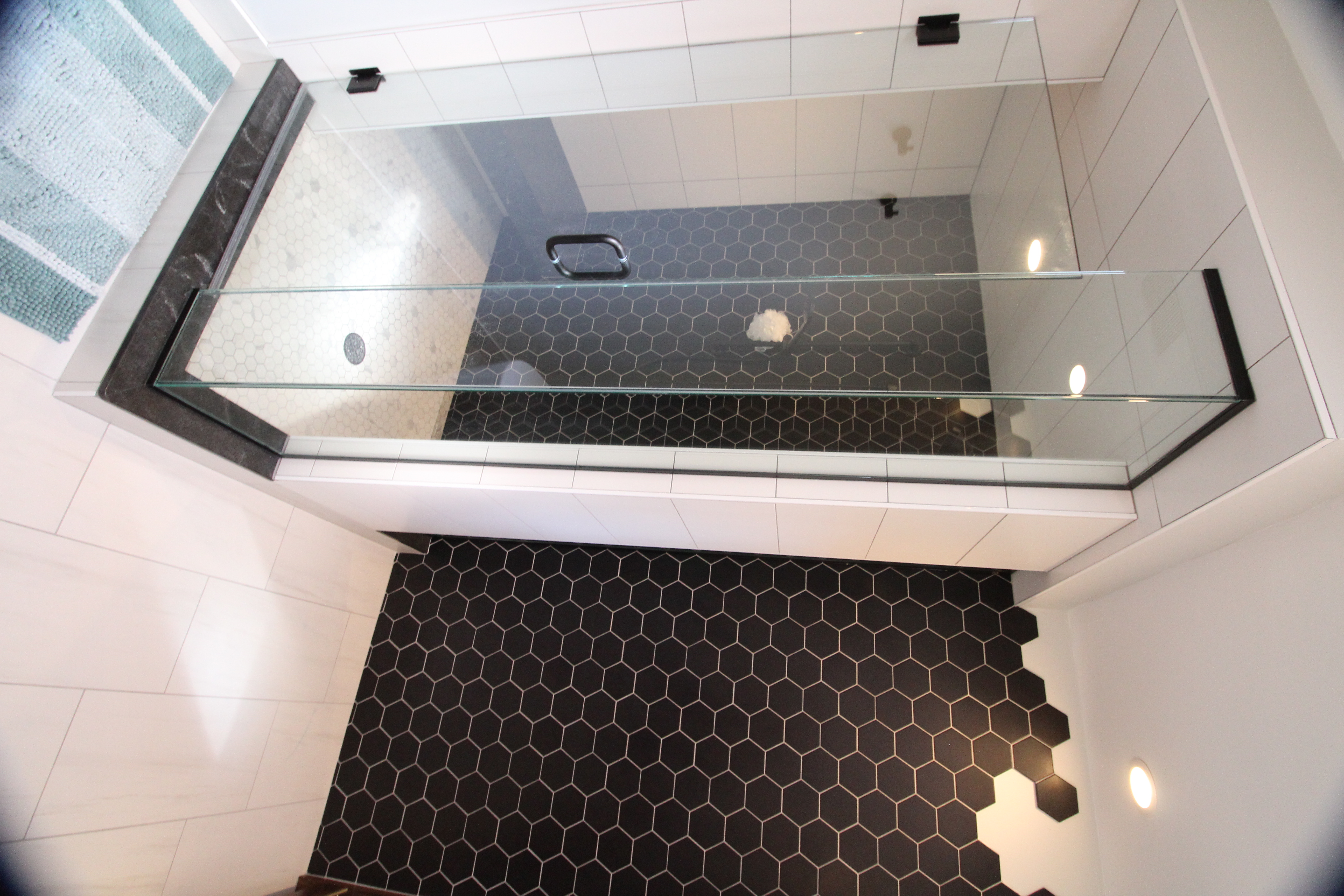 Glass shower enclosure with black hex tile feature wall and white tile surround.