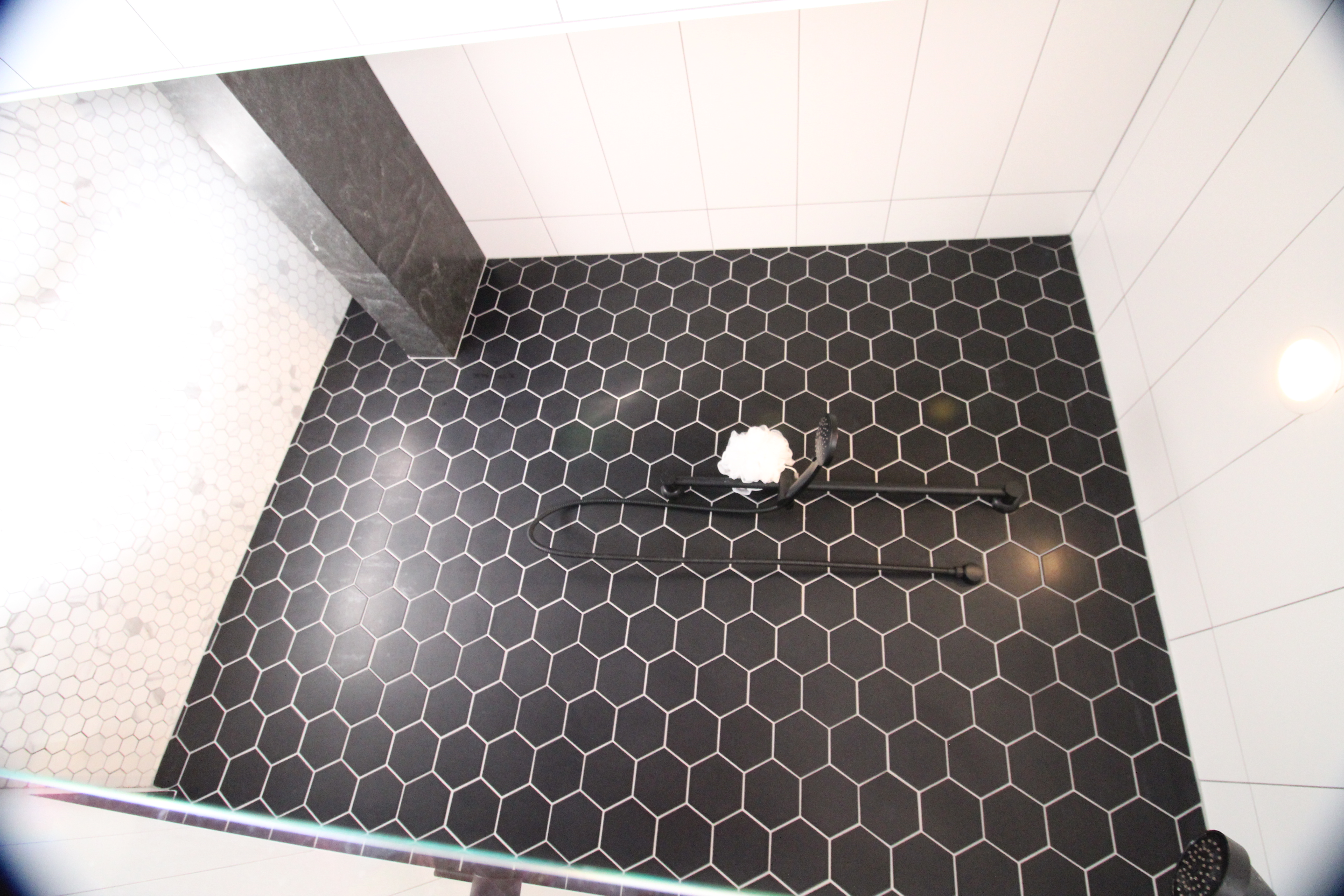 Shower interior with matte black fixtures, black hex tile wall, and built-in bench.