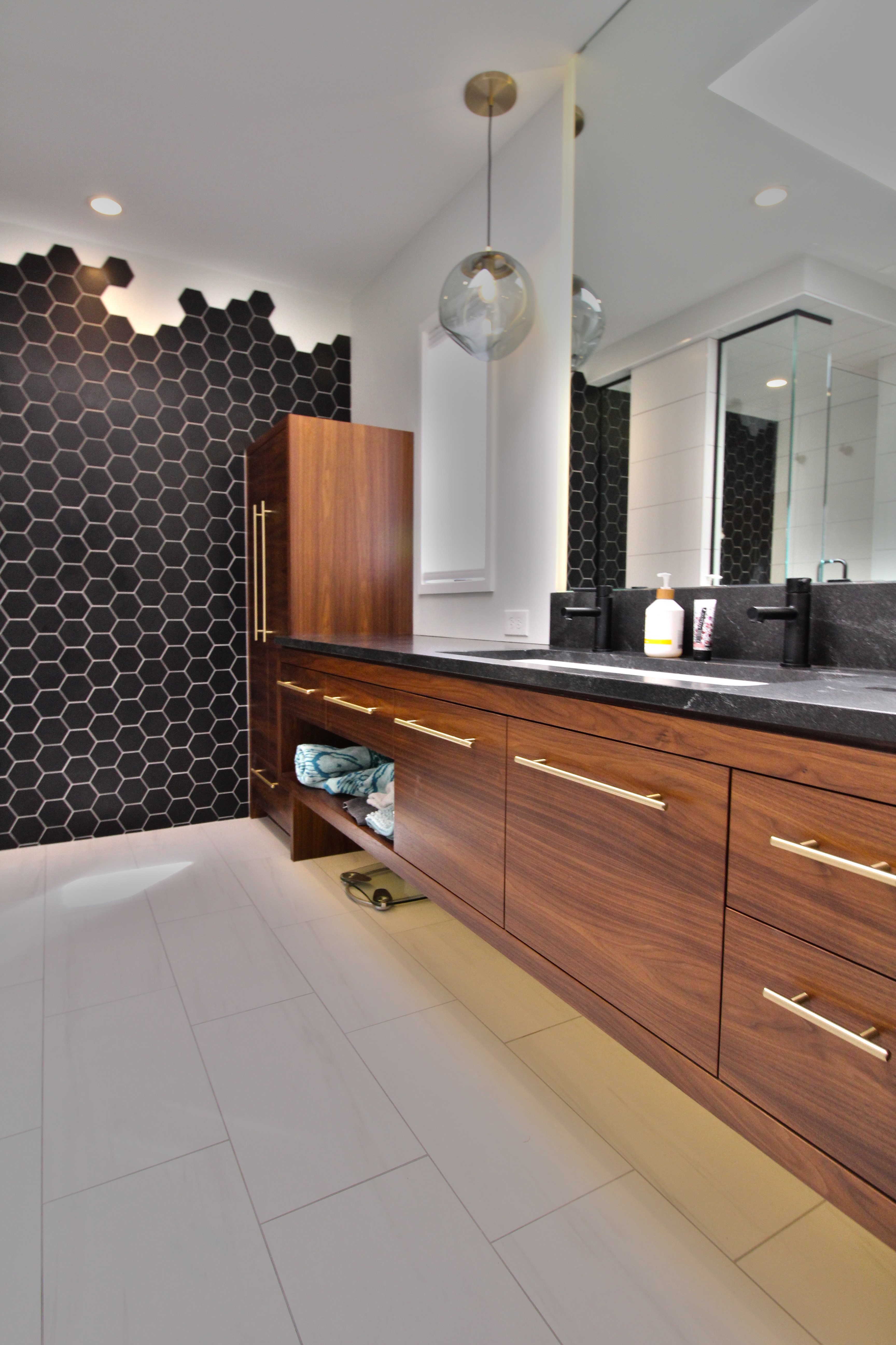 Close-up of walnut vanity with brass hardware, pendant lighting, and black hex tile backdrop.